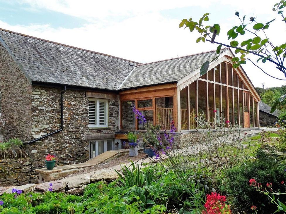 A stone house with large glass windows and a slate roof surrounded by plants and flowers at The Cider Barn at Home Farm in Down Thomas near Plymouth