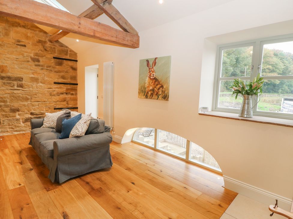 A sitting area with a gray sofa and cushions near a stone wall and windows with flowers at Morgans Barn in Honley