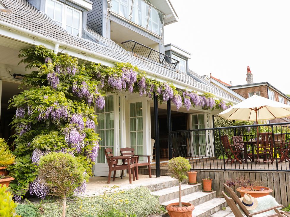 An outdoor patio with wooden chairs purple flowers growing along the roof and a large umbrella at Elphinstone in Newton Ferrers near Plymouth