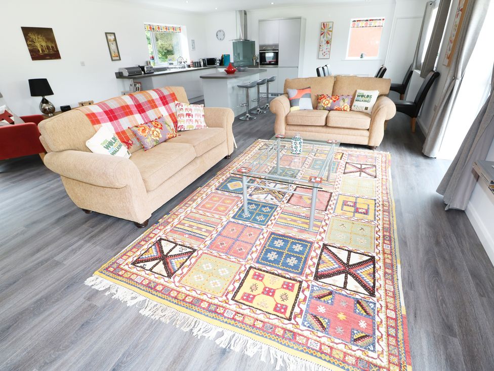 A living room with two beige sofas a glass coffee table and a colorful rug at Heron Lodge in Mavis Enderby near Spilsby
