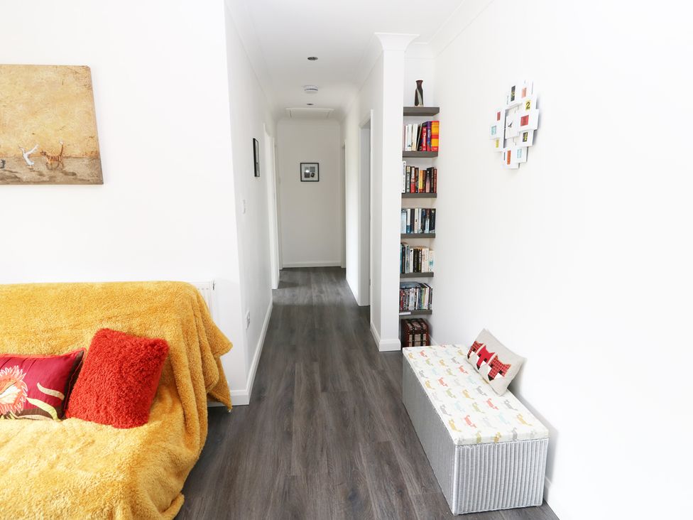 A hallway with a yellow covered sofa and red pillows a bookshelf and a storage bench with cushions at Heron Lodge in Mavis Enderby near Spilsby
