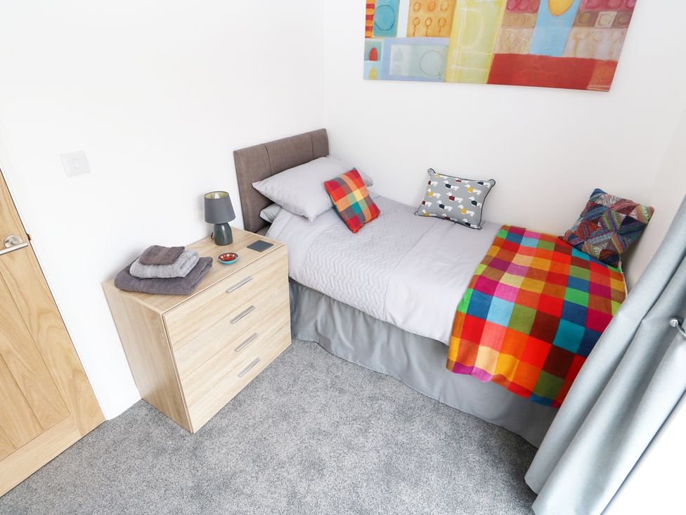 A small bedroom with a single bed with colorful pillows and a blanket and a wooden chest of drawers with a lamp and folded towels at Heron Lodge in Mavis Enderby near Spilsby