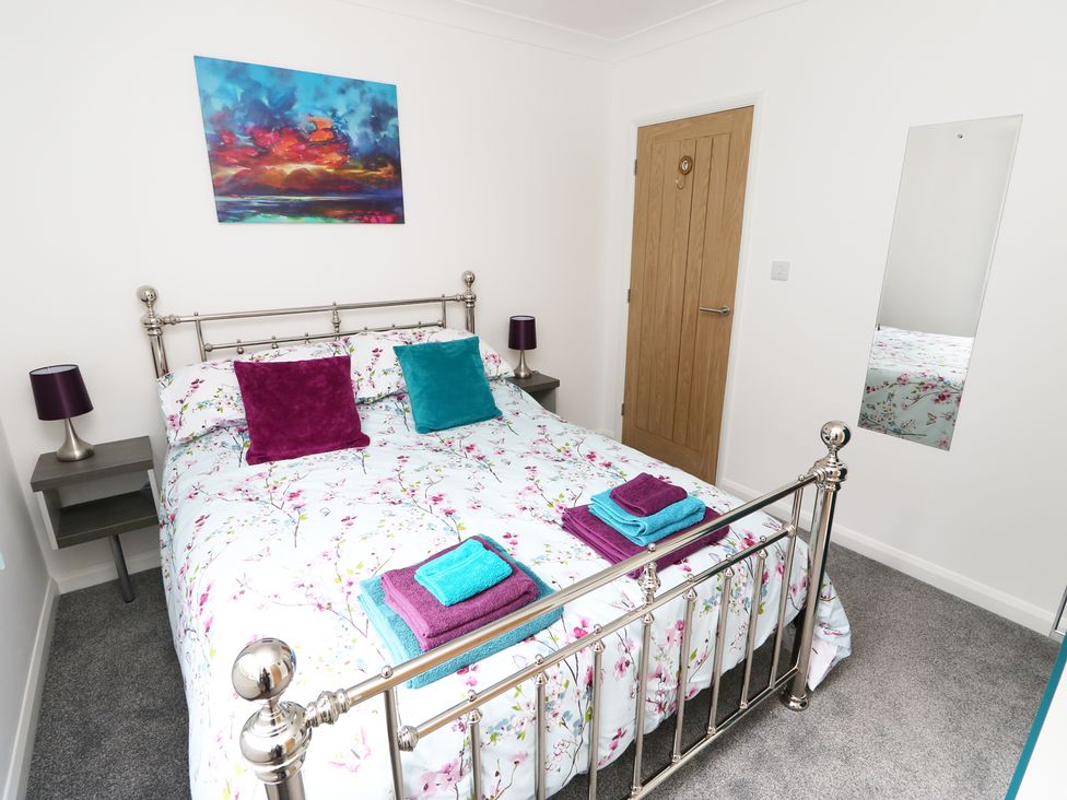 A bedroom with a metal bed frame floral bedding purple and teal pillows bedside tables with lamps a wooden door and a wall mirror at Heron Lodge in Mavis Enderby near Spilsby