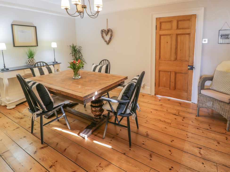 A dining room with a wooden table surrounded by black chairs with cushions next to a wooden door and a sideboard with lamps and plants at Bwthyn Morse in Llanfair