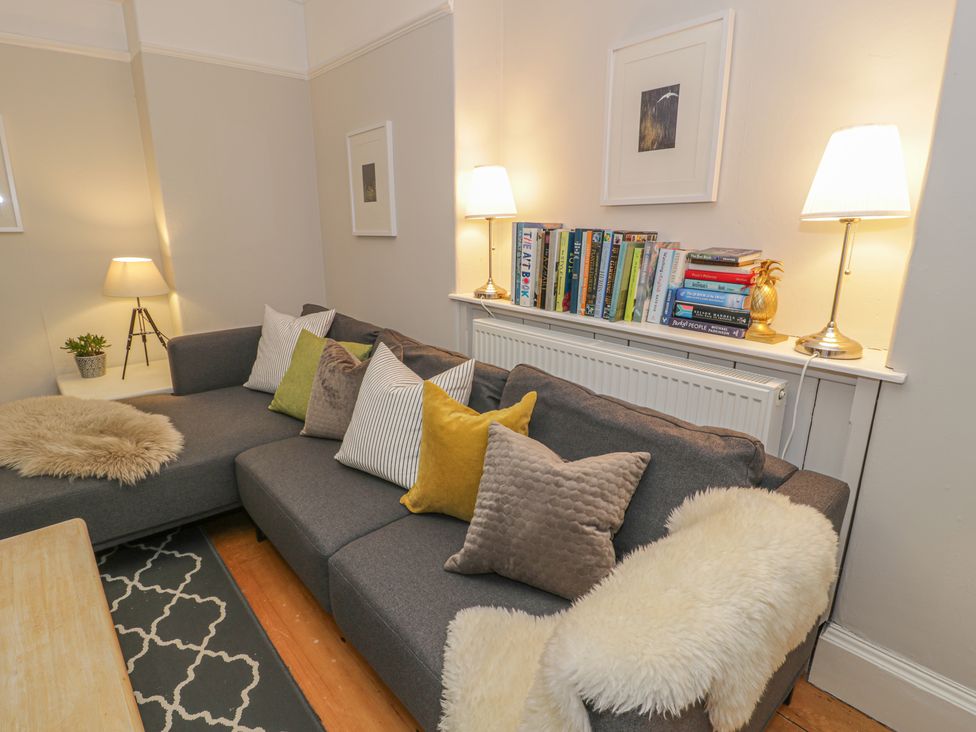 A living room with a gray sectional sofa with multiple pillows a bookshelf above a radiator and two table lamps at Bwthyn Morse in Llanfair
