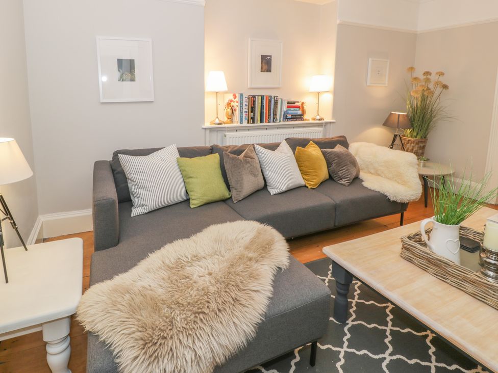 A living room with a grey sectional sofa with multiple cushions a wooden coffee table with a tray and plants and lamps creating a cozy setting at Bwthyn Morse in Llanfair