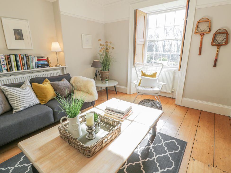 A living room with a gray sofa and pillows a wooden coffee table and books at Bwthyn Morse in Llanfair