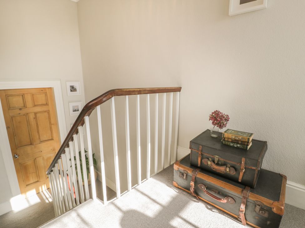A staircase landing with two vintage suitcases stacked and books with a flower vase on top at Bwthyn Morse in Llanfair