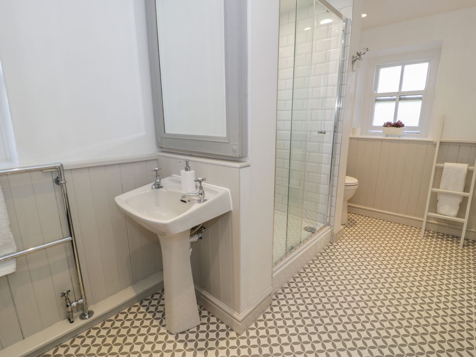 A bathroom with a pedestal sink mirror glass shower enclosure toilet towel rack and patterned floor tiles at Bwthyn Morse in Llanfair