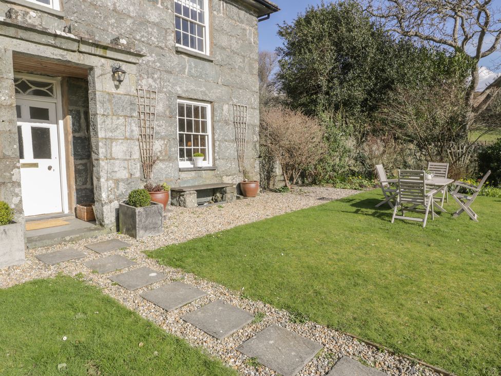 A stone house with a white door a gravel path stone bench potted plants and outdoor table with chairs on grass at Bwthyn Morse in Llanfair