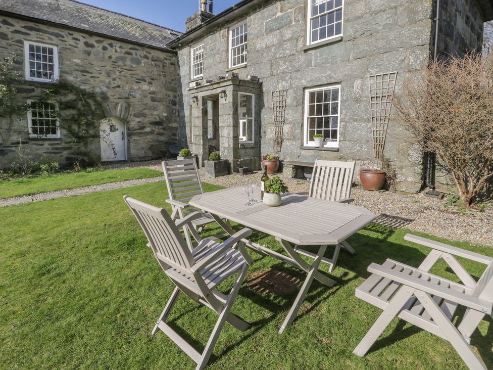 A garden area with wooden table and chairs on grass near a stone building at Bwthyn Morse in Llanfair