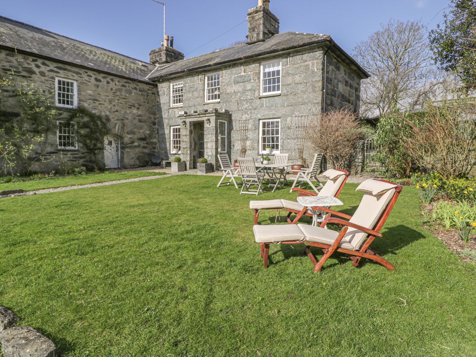 A garden with lawn chairs and a table set in front of a stone house at Bwthyn Morse in Llanfair