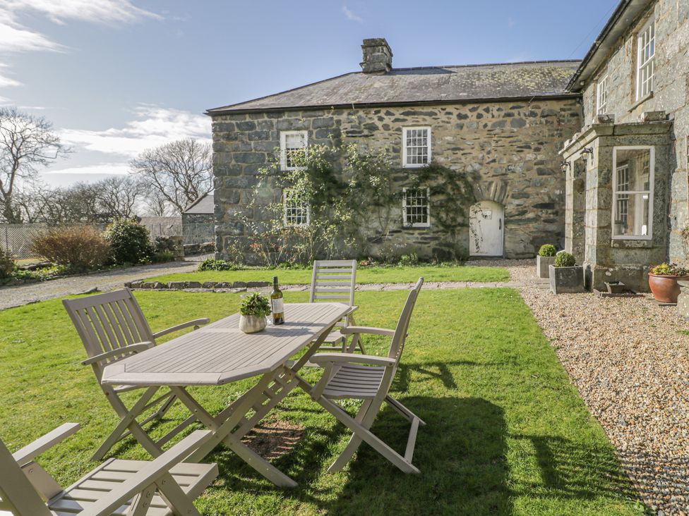 A patio table with chairs on a lawn in front of a stone building at Bwthyn Morse in Llanfair