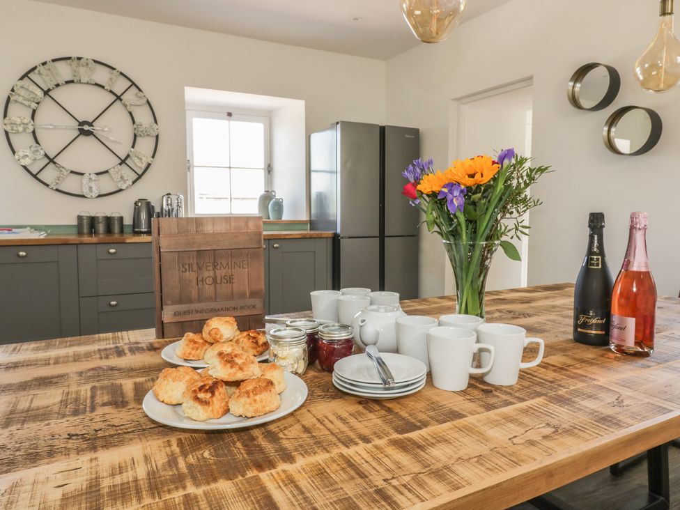 A kitchen with a wooden table set with scones cups plates jars flowers and bottles at Silvermine House in Charlestown