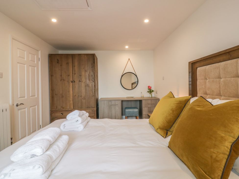A bedroom with a bed with mustard pillows towels on the bed a wooden wardrobe a desk with a round mirror and a stool at Silvermine House in Charlestown