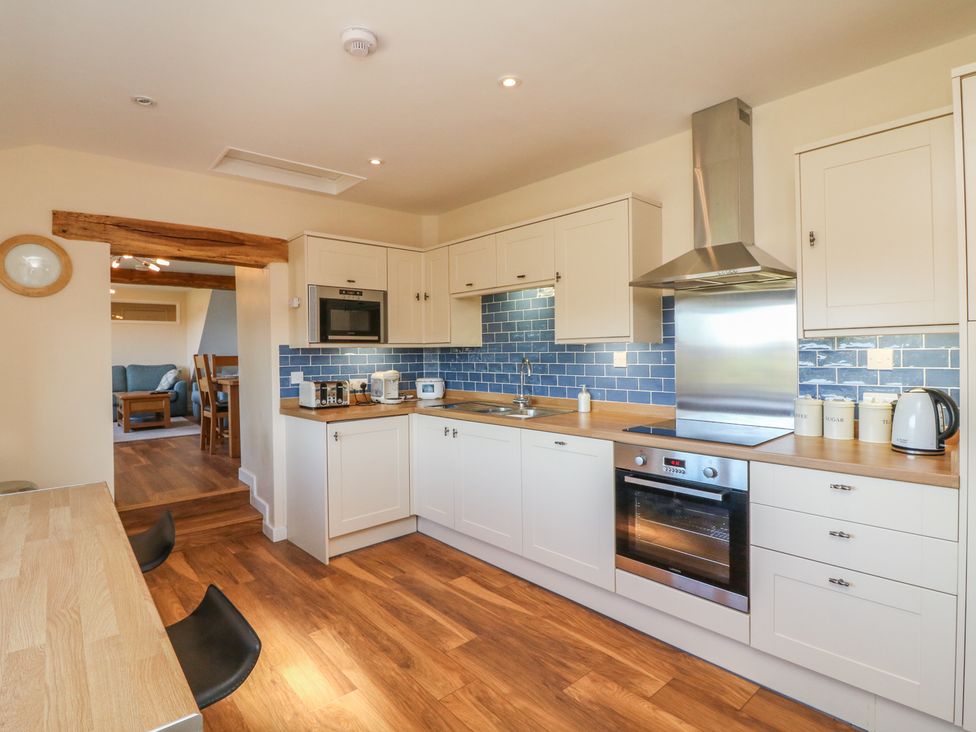 A kitchen with white cabinets blue tiled backsplash and wooden counters next to a dining area at Rose Cottage in Barnstaple