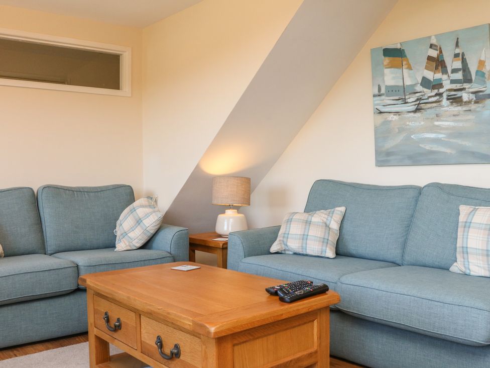 A living room with two blue sofas a wooden coffee table with remote controls a side table with a lamp and a painting of sailboats on the wall at Rose Cottage in Barnstaple