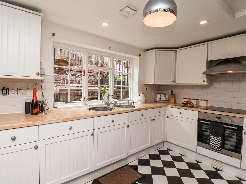 A kitchen with white cabinets wooden countertop black and white checkered floor and a window overlooking a patio at Midships Cottage in Whitby