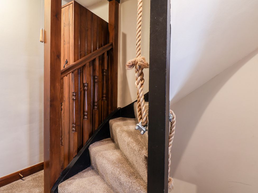 A carpeted staircase with wooden railing and a hanging rope at Midships Cottage in Whitby