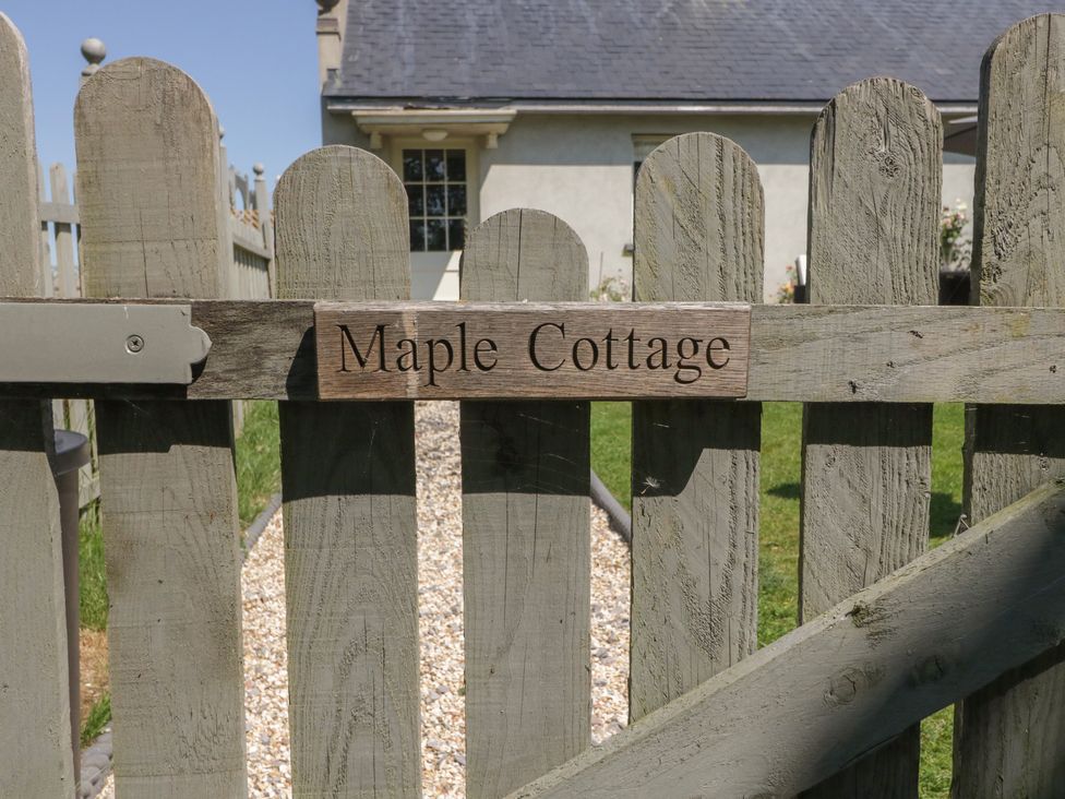 A wooden gate with a sign that reads Maple Cottage and a house with a gravel path behind the gate at Maple Cottage in Buckland Newton near Dorchester