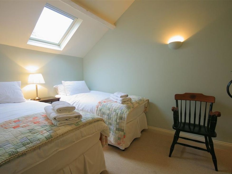 A bedroom with two single beds a wooden chair a bedside table with a lamp and a skylight window at Cider Press Cottage in Priston Village Bath