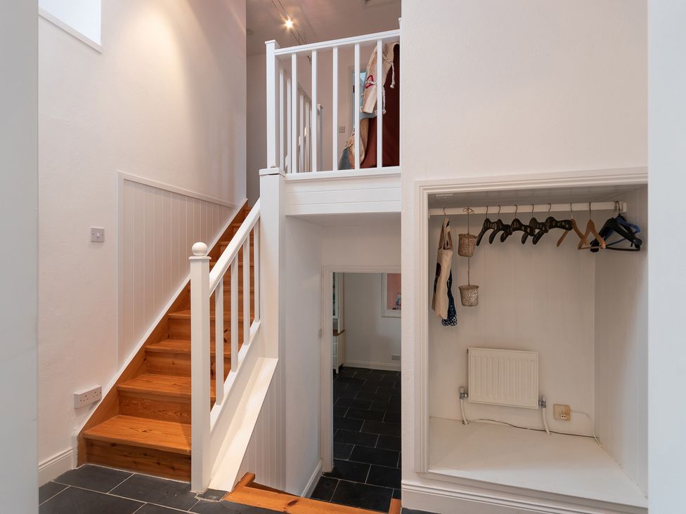 A stairwell with wooden steps and white railings next to a small closet with hangers at The Schooner in Goleen County Cork