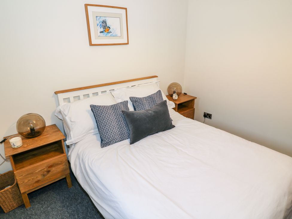 A bedroom with a white bed and three pillows two bedside tables with lamps and a picture of a bird on the wall at Kestrel Lodge in Dumfries