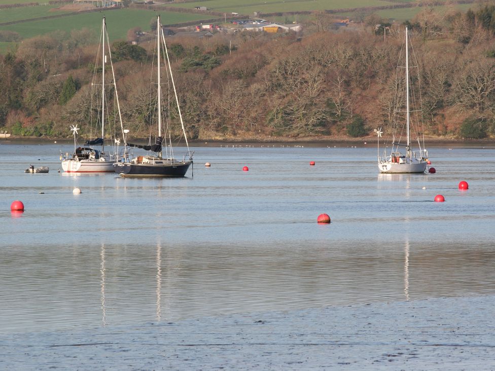 A body of water with three sailboats and red buoys with trees and fields in the background at The Daffodil Shed in Bere Alston