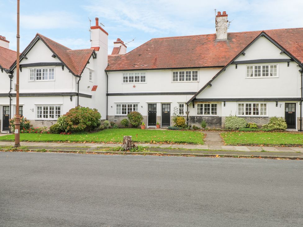 A row of white two-story houses with red tile roofs and green lawns with bushes at Sunlight Soap Cottage in Port Sunlight