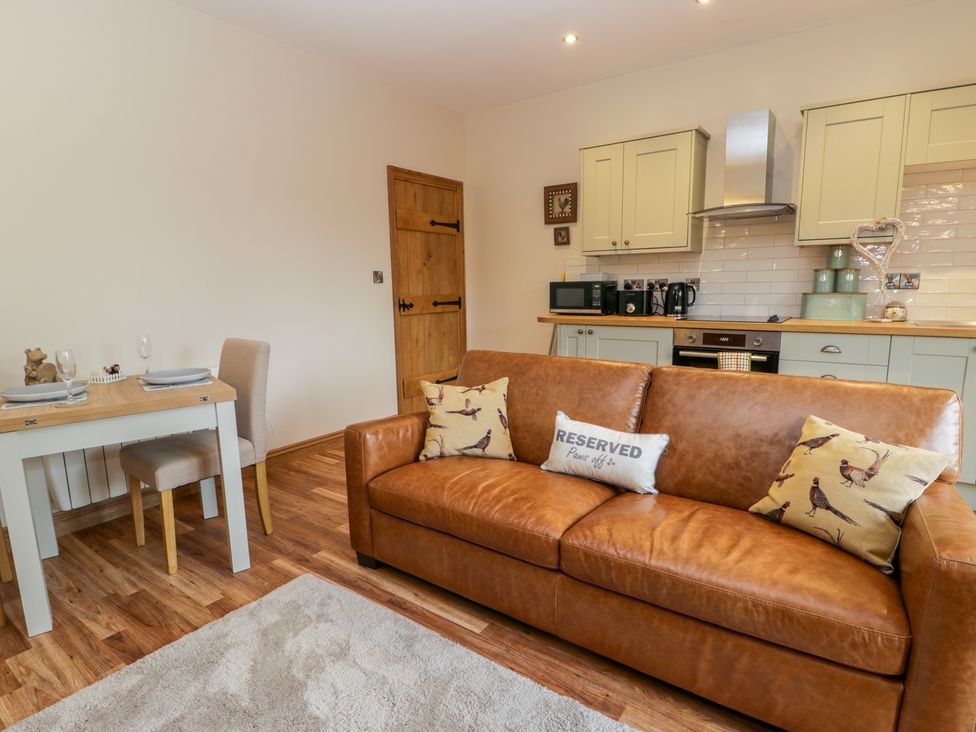 A kitchen and dining area with a brown leather sofa pillows a wooden table and chairs and kitchen cabinets at Wagtail Nest Northfield Cottage Scalby