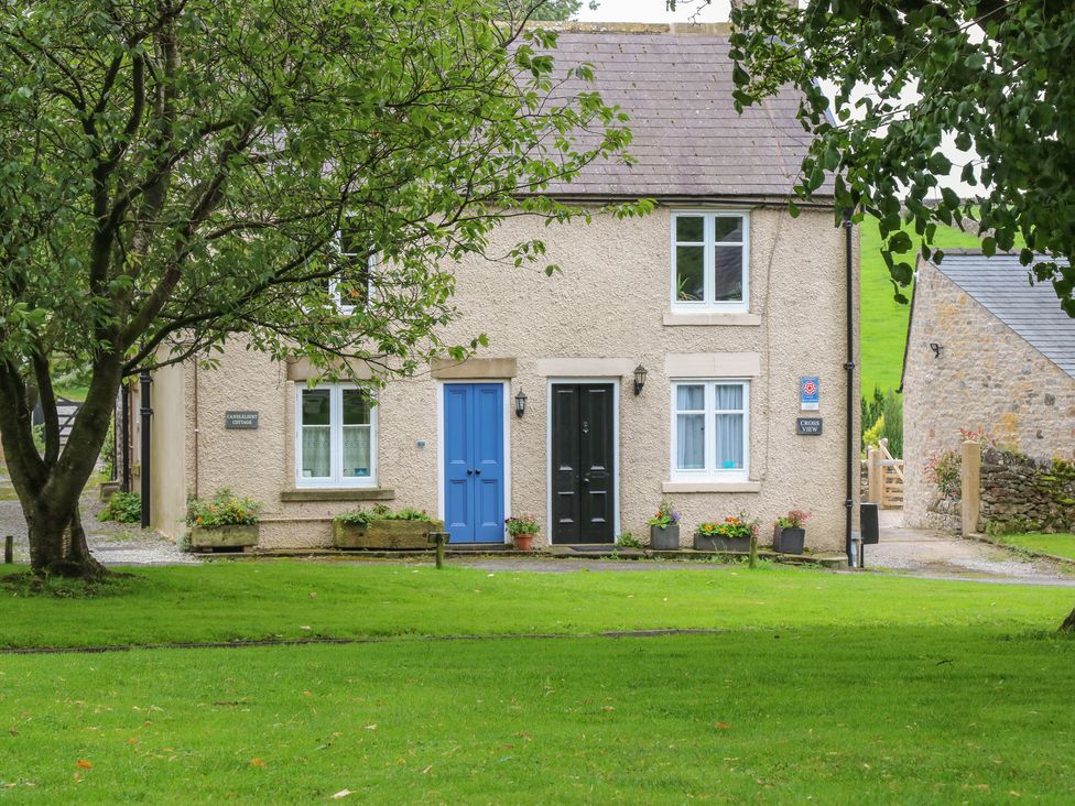 A cottage with a blue and a black door surrounded by grass trees and flowers at Candlelight Cottage in Litton Derbyshire