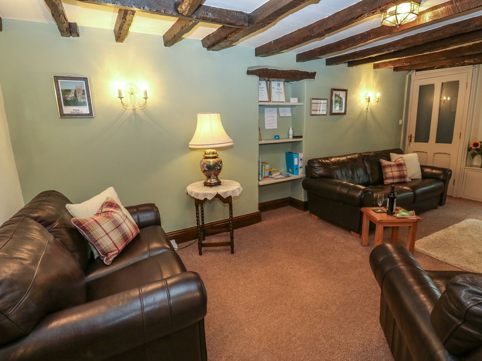 A living room with leather sofas wooden beams on ceiling a lamp on side table and a small wooden coffee table at Candlelight Cottage in Litton Derbyshire