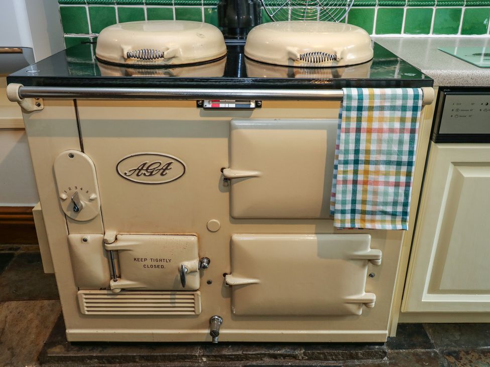 A cream colored aga cooker with lids on top and a checkered towel hanging on the handle in a kitchen at Candlelight Cottage in Litton Derbyshire
