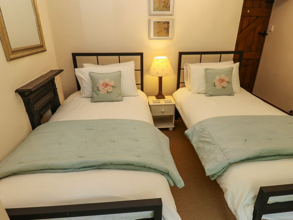 A bedroom with two single beds a nightstand with a lamp and a wooden door at Candlelight Cottage in Litton Derbyshire