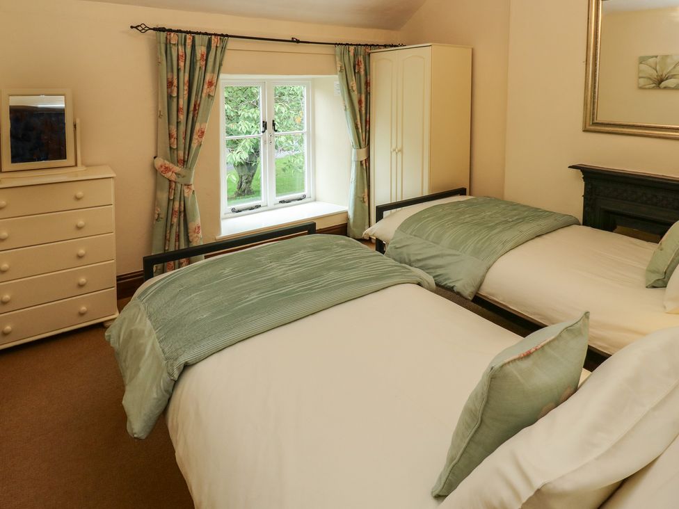 A bedroom with two single beds a chest of drawers a wardrobe and a window with floral curtains at Candlelight Cottage in Litton Derbyshire