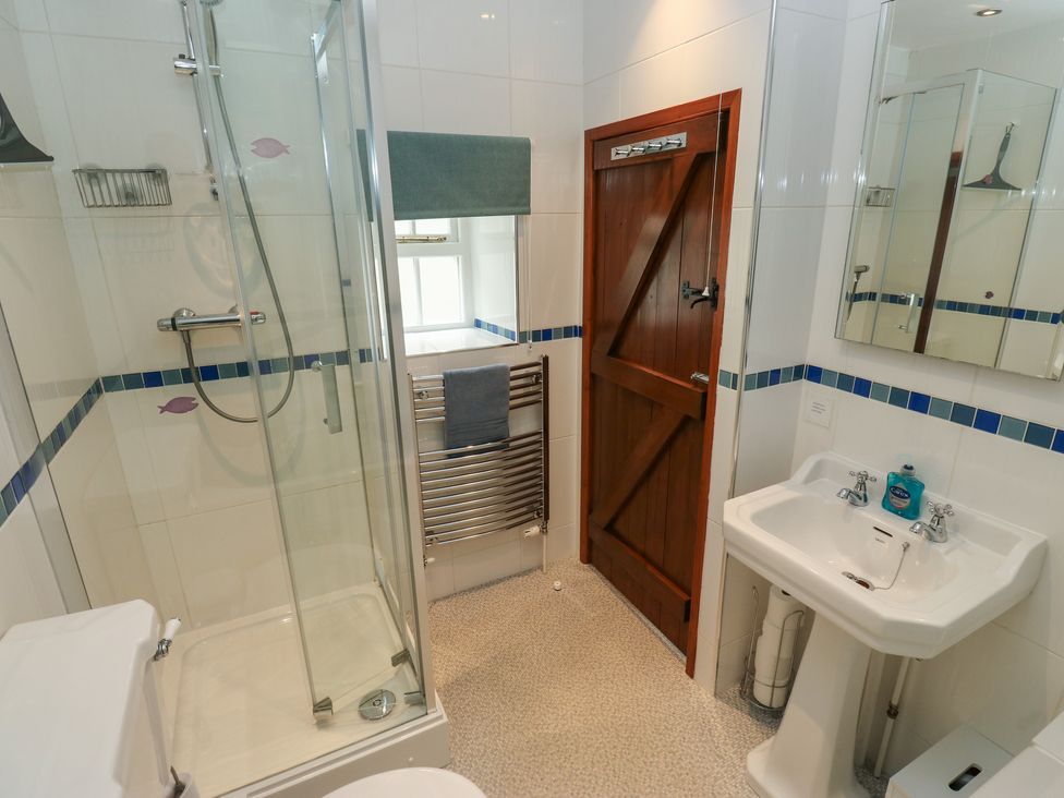 A bathroom with a shower enclosure a sink with mirror a towel rail and a wooden door at Candlelight Cottage in Litton Derbyshire