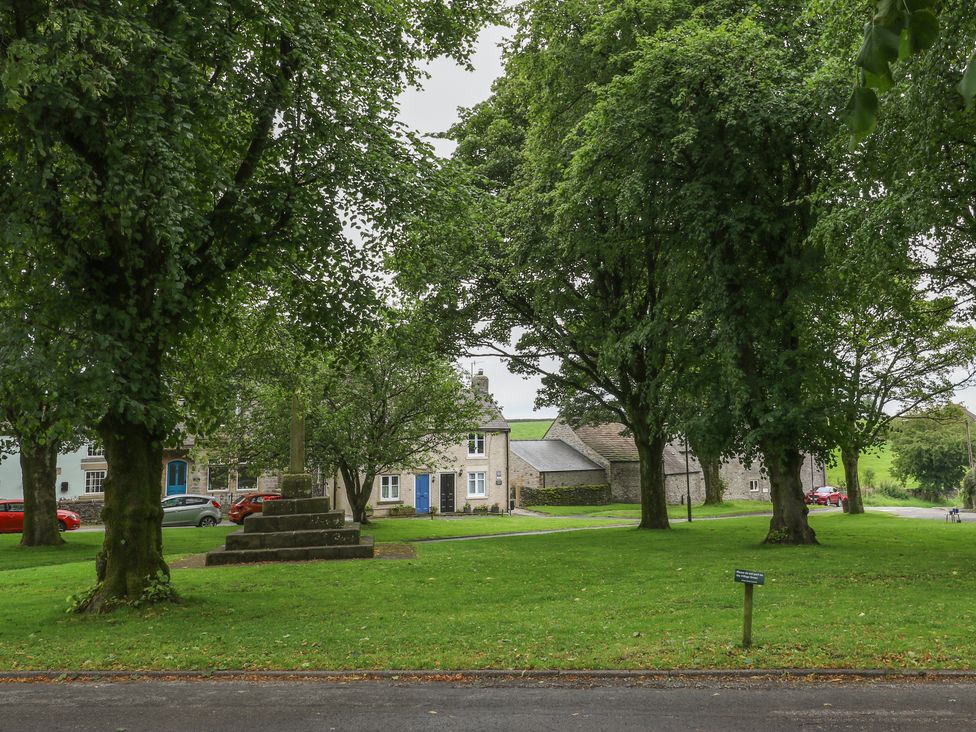 A small village green with large trees and a stone monument with houses in the background at Candlelight Cottage in Litton Derbyshire