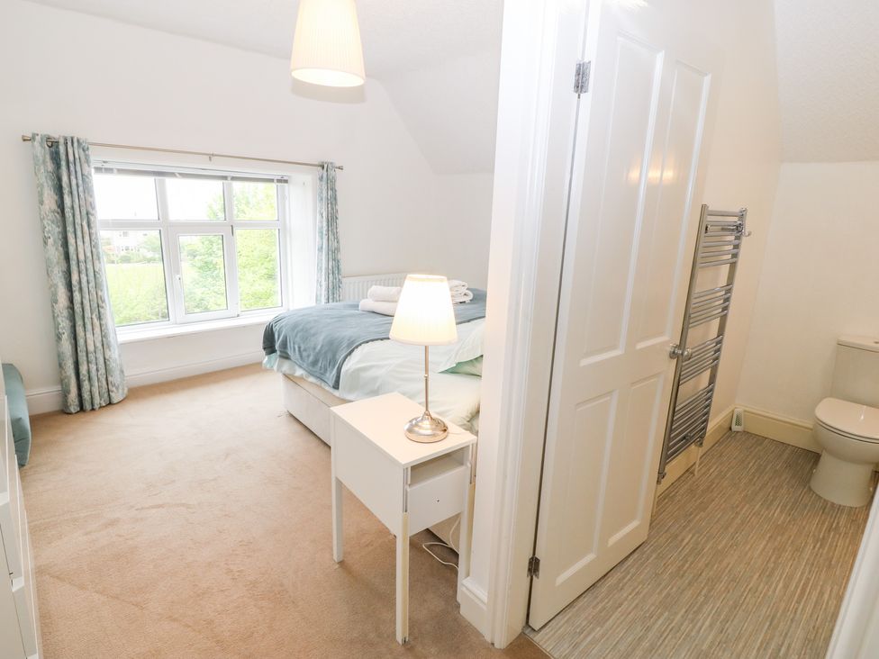 A bedroom with a bed a nightstand with lamp next to an open door leading to a bathroom at Flat 3 Ty Clyd in Criccieth