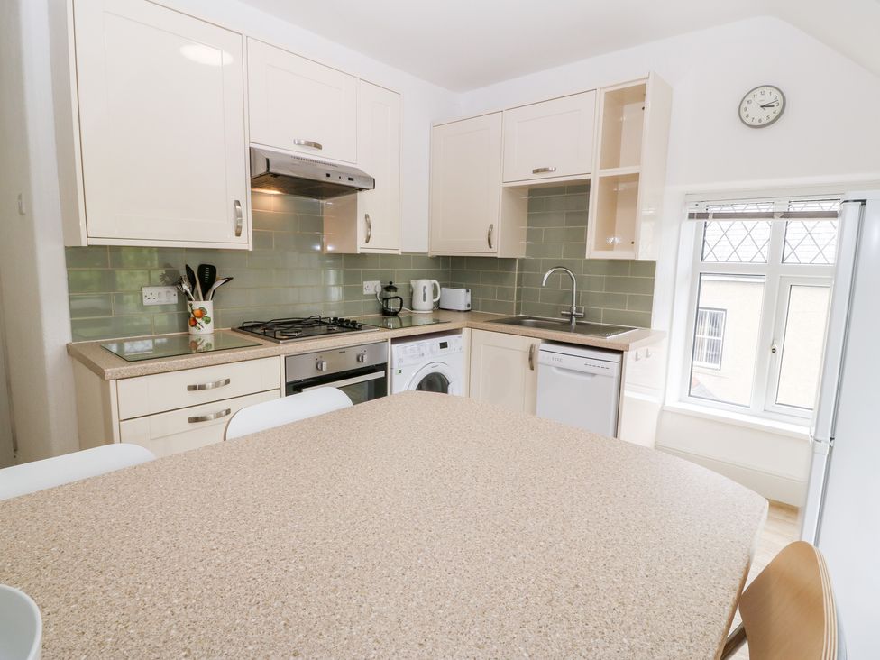 A kitchen with white cabinets a washing machine an oven a stove a sink and a window at Flat 3 Ty Clyd in Criccieth