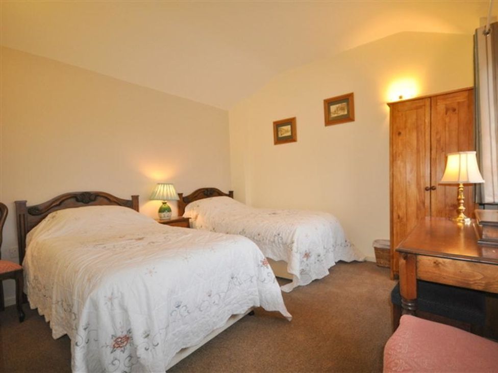 A bedroom with two single beds bedside table lamps wooden wardrobe and a desk at Follis Cottage in Nottington