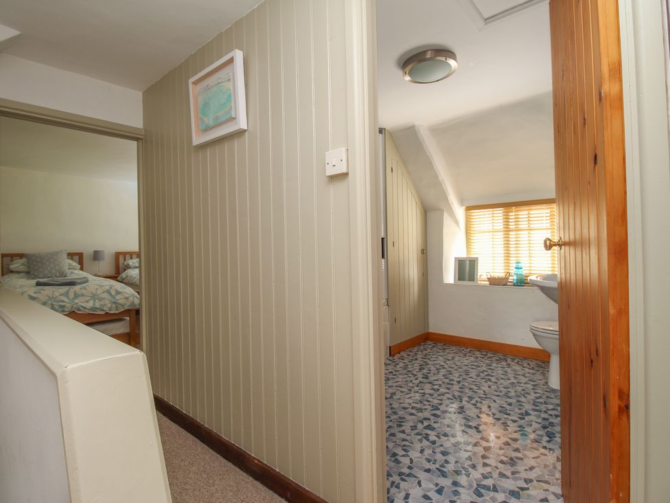 A hallway showing a bedroom with two beds and a bathroom with tiled floor at Forge Cottage in West Lulworth