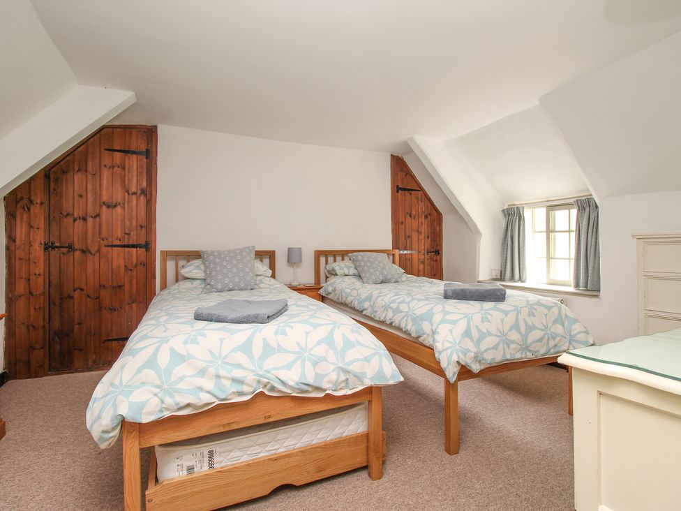 A bedroom with two single beds wooden doors and a window at Forge Cottage in West Lulworth