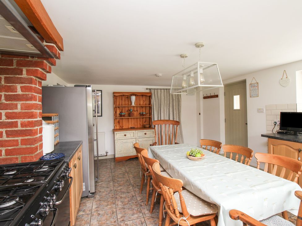 A kitchen dining area with a long table and wooden chairs a brick chimney a refrigerator and wooden cabinets at Forge Cottage in West Lulworth