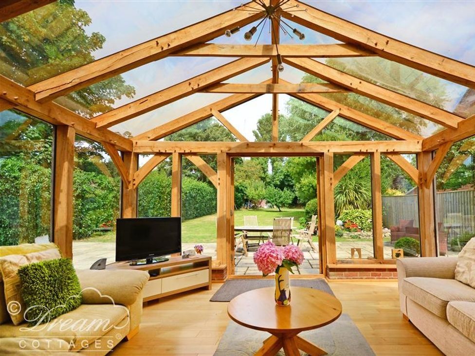 A sunroom with wooden beams glass walls a television on a stand and sofas around a wooden coffee table with flowers at Fossil Barn in Weymouth