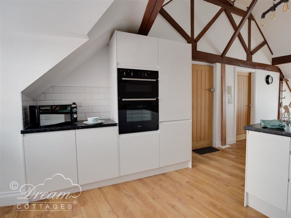 A kitchen with white cabinets black countertop a microwave oven and wooden doors at Old Coastguard Apartment 3 in Weymouth