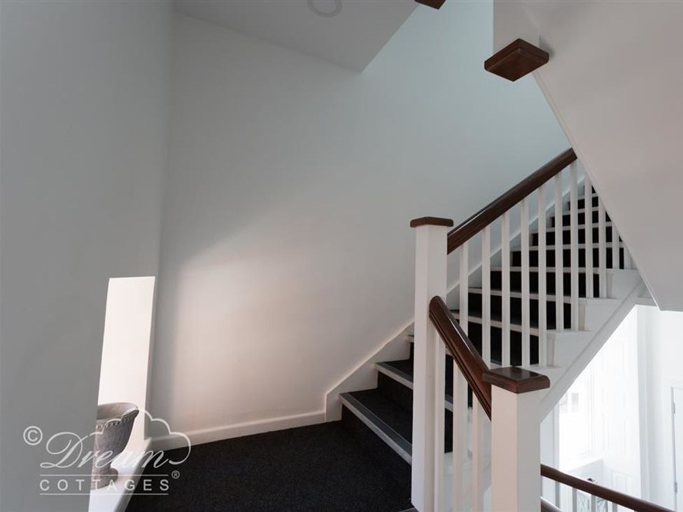A stairway with white walls dark carpet and wooden handrails at Old Coastguard Apartment 3 in Weymouth