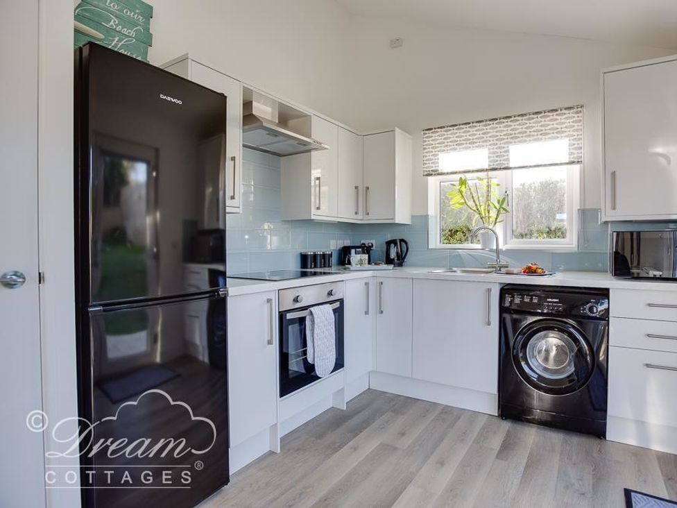 A kitchen with a black refrigerator oven washing machine and cabinets at Outlook Lodge in Bowleaze