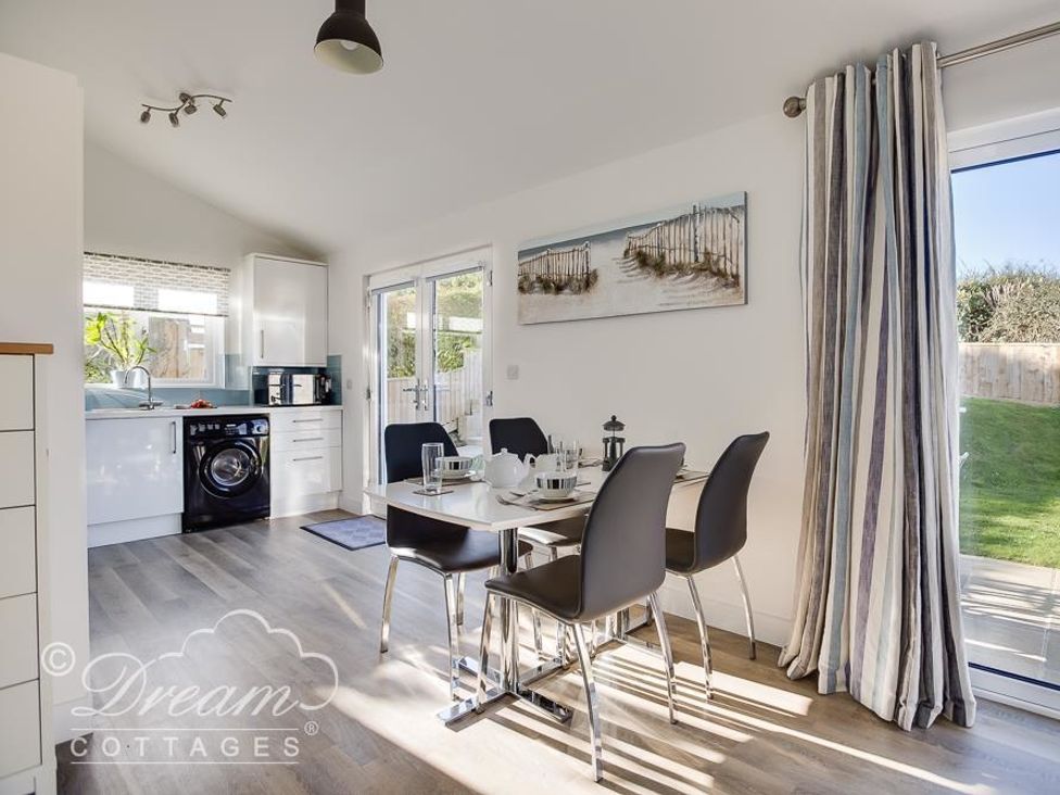 A dining area with a table and four chairs next to a kitchen with white cabinets and a washing machine at Outlook Lodge in Bowleaze