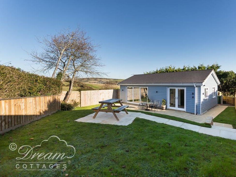 A blue cottage with a picnic table and metal patio furniture in a fenced grassy yard at Outlook Lodge in Bowleaze