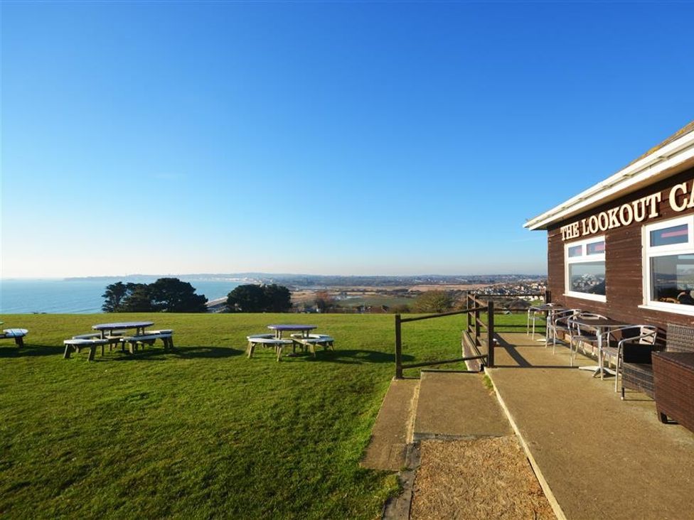 An outdoor seating area with picnic tables on grass near a building with a view of the coast at Outlook Lodge in Bowleaze